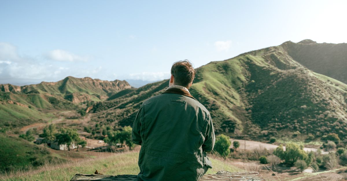 Person resting on a wooden bench facing a rural landscape